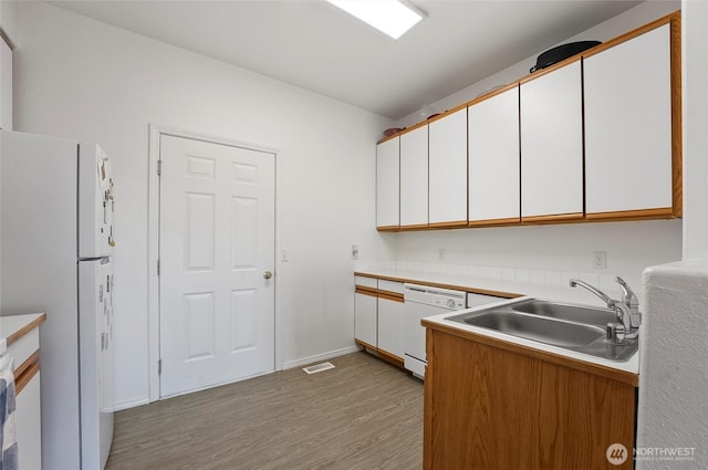 kitchen with visible vents, light wood-style floors, white cabinetry, a sink, and white appliances