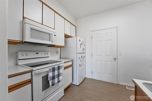 kitchen with light wood-style flooring, white appliances, visible vents, white cabinets, and light countertops