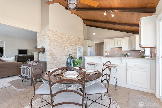 dining space with a wood stove, light tile patterned floors, wood ceiling, and beamed ceiling