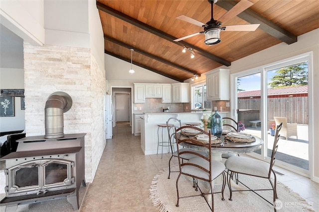 dining room featuring beam ceiling, a ceiling fan, a wood stove, light tile patterned flooring, and wooden ceiling