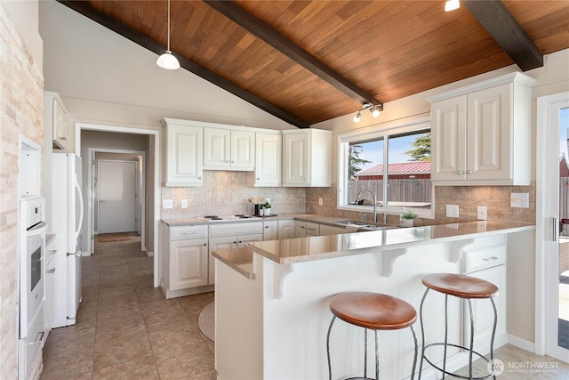 kitchen with tasteful backsplash, a sink, white appliances, a peninsula, and a kitchen breakfast bar