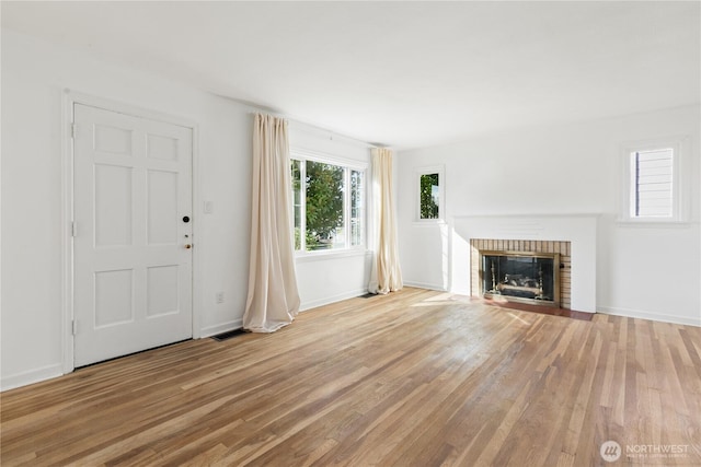 unfurnished living room with visible vents, baseboards, light wood-style floors, and a brick fireplace