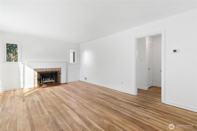 unfurnished living room featuring light wood finished floors, plenty of natural light, a brick fireplace, and baseboards