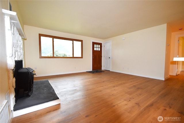 unfurnished living room with visible vents, hardwood / wood-style floors, a wood stove, and baseboards