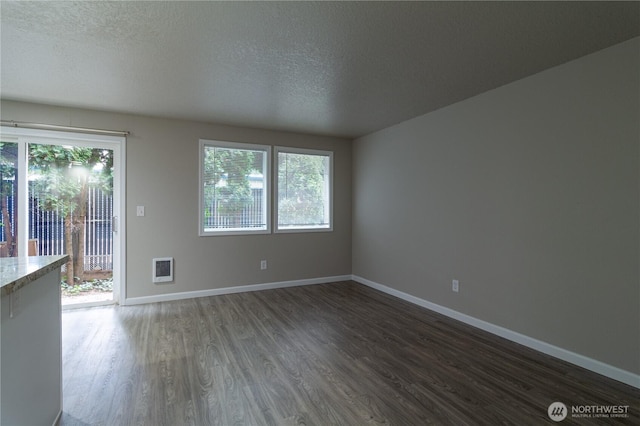 spare room featuring heating unit, baseboards, dark wood-style flooring, and a textured ceiling