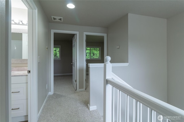 hallway featuring an upstairs landing, visible vents, light colored carpet, and baseboards