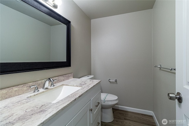 bathroom featuring toilet, vanity, baseboards, and wood finished floors