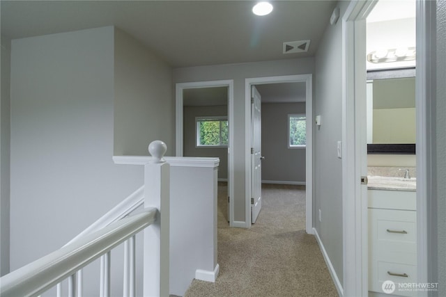 hallway featuring an upstairs landing, visible vents, light carpet, and baseboards