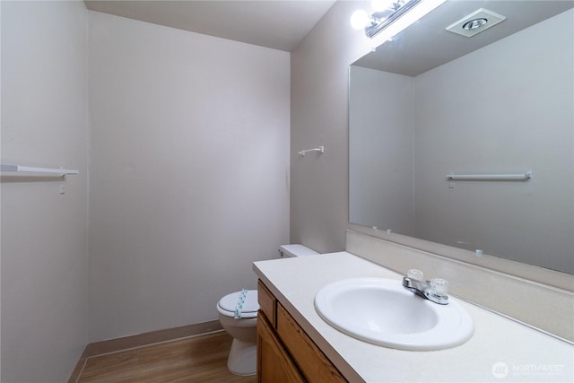 half bath featuring vanity, toilet, wood finished floors, and baseboards