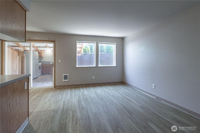 unfurnished living room with heating unit, baseboards, and wood finished floors