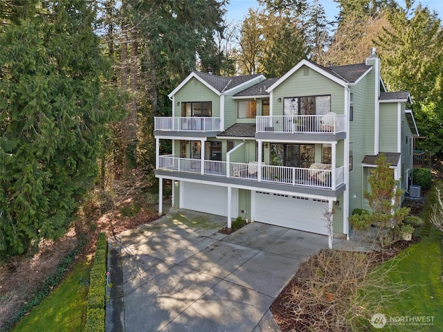 view of front facade with a chimney, an attached garage, concrete driveway, and a balcony