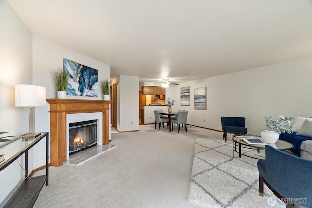 living area with a glass covered fireplace, light colored carpet, baseboards, and ceiling fan