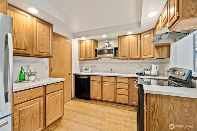 kitchen featuring under cabinet range hood, light countertops, appliances with stainless steel finishes, light wood-style floors, and a sink