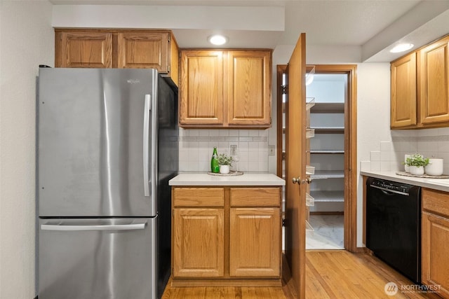 kitchen with decorative backsplash, black dishwasher, light countertops, and freestanding refrigerator