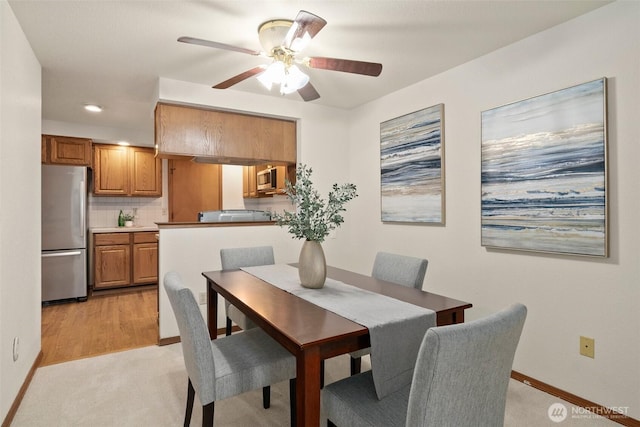 dining area featuring a ceiling fan, light colored carpet, and baseboards