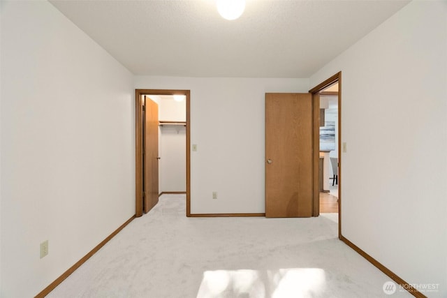 unfurnished bedroom featuring a walk in closet, baseboards, a closet, and light carpet