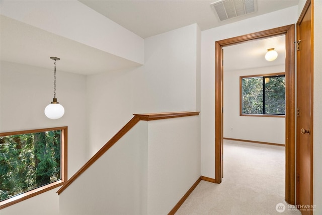 hallway featuring an upstairs landing, visible vents, light carpet, and baseboards