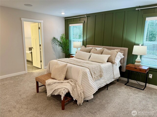 carpeted bedroom featuring baseboards, ensuite bathroom, and a decorative wall