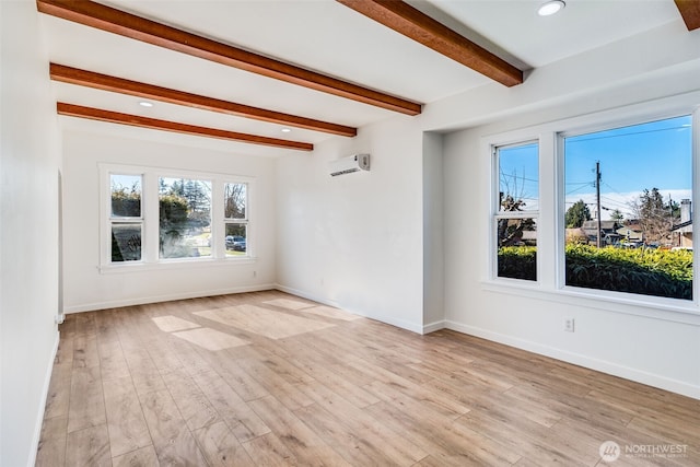 unfurnished room with beamed ceiling, a wall unit AC, light wood-style flooring, and baseboards