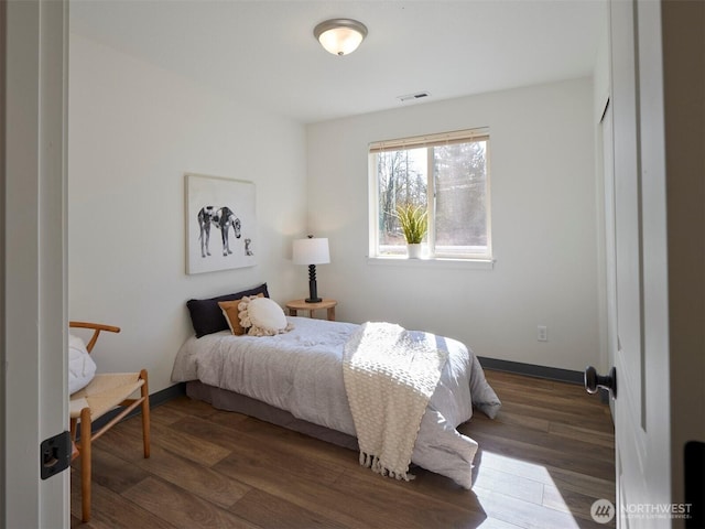 bedroom with baseboards, visible vents, and wood finished floors