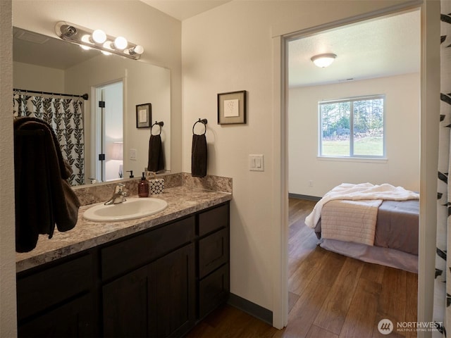 full bath featuring ensuite bathroom, wood finished floors, vanity, and baseboards