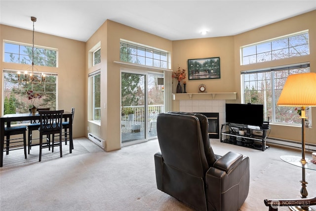 living room with a tiled fireplace, a notable chandelier, a baseboard heating unit, and carpet floors