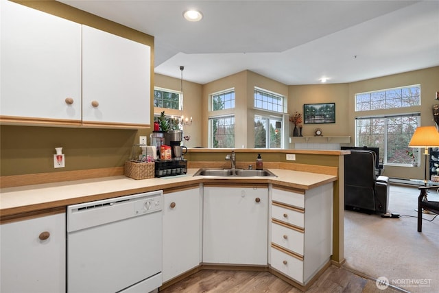 kitchen with light countertops, a peninsula, white dishwasher, white cabinetry, and a sink