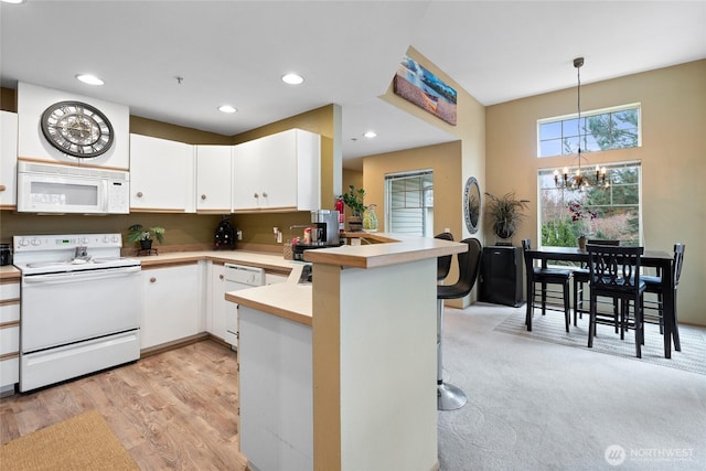 kitchen with white appliances, a peninsula, white cabinets, light countertops, and a chandelier