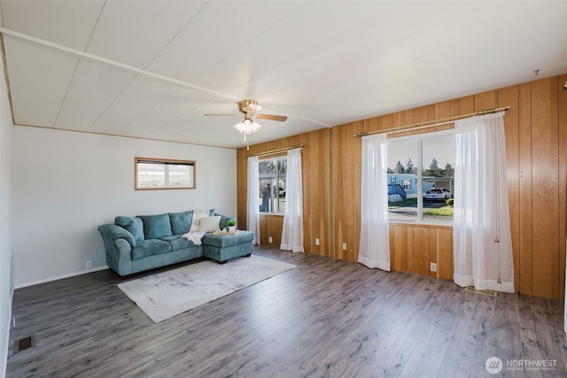 unfurnished living room with visible vents, ceiling fan, wood walls, wood finished floors, and baseboards