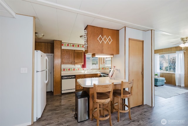 kitchen with a peninsula, white appliances, brown cabinetry, and dark wood-style flooring