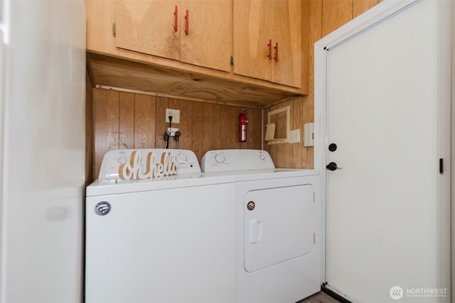 laundry room featuring washing machine and dryer, cabinet space, and wooden walls