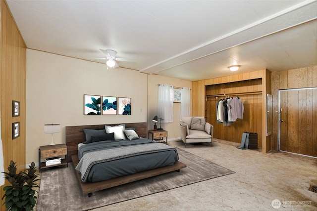 carpeted bedroom featuring ceiling fan, wooden walls, and a closet