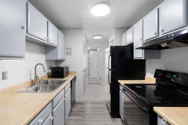 kitchen featuring light wood finished floors, under cabinet range hood, light countertops, black appliances, and a sink