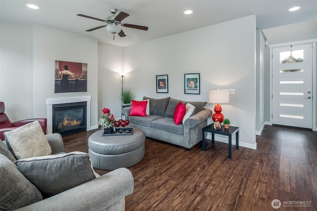 living area featuring a glass covered fireplace, recessed lighting, wood finished floors, and baseboards