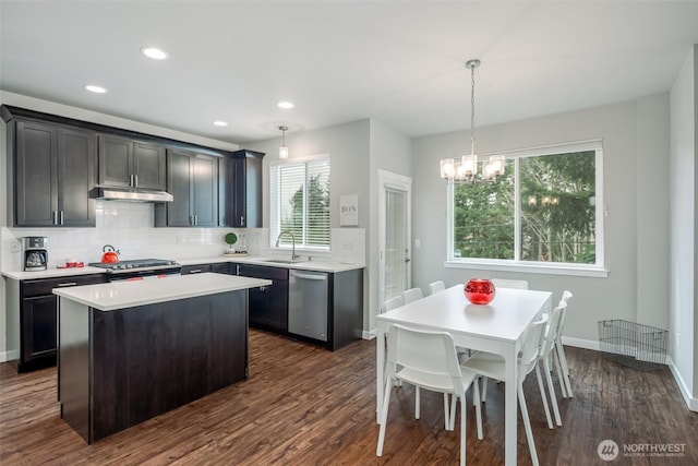 kitchen with backsplash, a kitchen island, under cabinet range hood, stainless steel dishwasher, and a sink