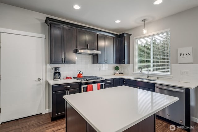 kitchen featuring backsplash, under cabinet range hood, light countertops, appliances with stainless steel finishes, and a sink