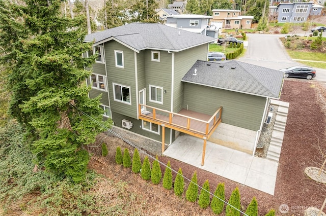 back of house with a wooden deck, roof with shingles, and driveway