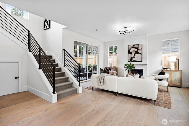 living room featuring a large fireplace, baseboards, stairway, and light wood finished floors