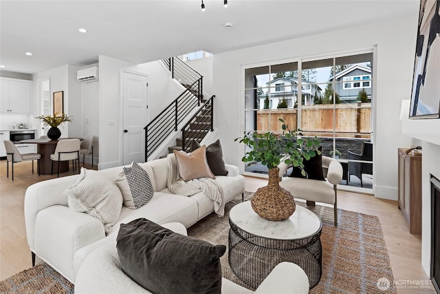 living room featuring recessed lighting, light wood-style flooring, stairway, an AC wall unit, and baseboards