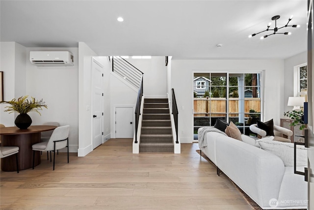 living area with a wall unit AC, light wood-type flooring, stairs, and a notable chandelier