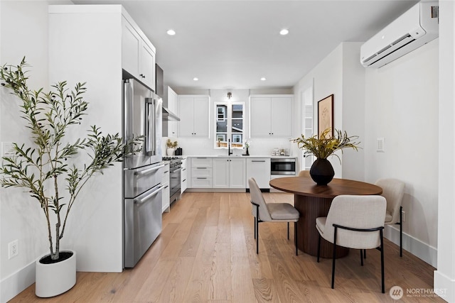 kitchen featuring a sink, high quality appliances, white cabinetry, an AC wall unit, and light wood finished floors