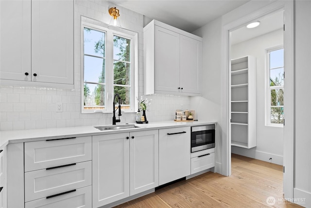 kitchen featuring light countertops, stainless steel microwave, backsplash, a sink, and light wood-type flooring