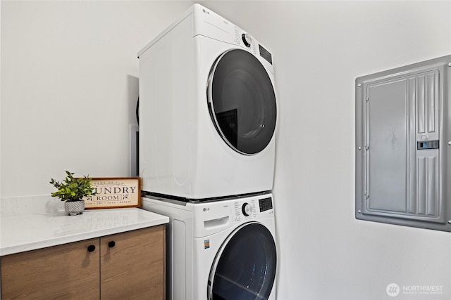 laundry area featuring electric panel, cabinet space, and stacked washing maching and dryer