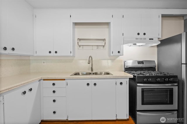 kitchen featuring light countertops, under cabinet range hood, stainless steel range with gas cooktop, white cabinetry, and a sink