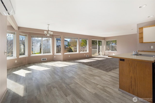 interior space featuring visible vents, an inviting chandelier, a sink, light wood-style floors, and a wall mounted air conditioner