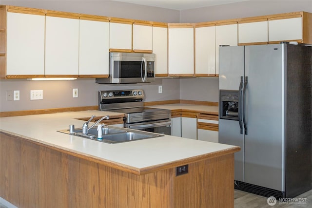 kitchen featuring a sink, stainless steel appliances, a peninsula, and light countertops