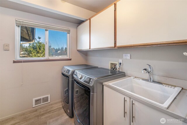 washroom with visible vents, light wood-type flooring, a sink, cabinet space, and washing machine and clothes dryer