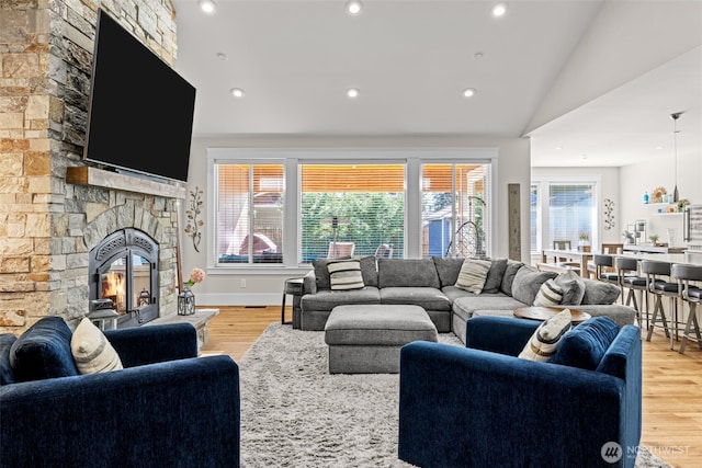 living room with lofted ceiling, a stone fireplace, recessed lighting, and light wood-style floors