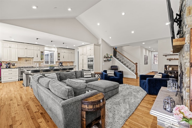 living area with light wood-style flooring, recessed lighting, high vaulted ceiling, and stairway