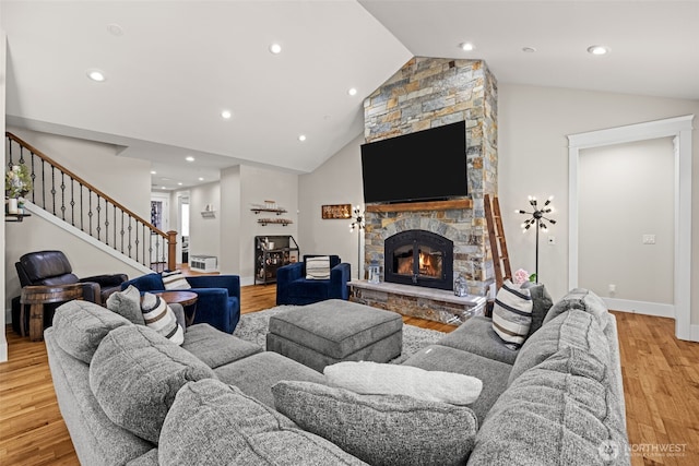 living area featuring light wood finished floors, lofted ceiling, stairway, a stone fireplace, and recessed lighting